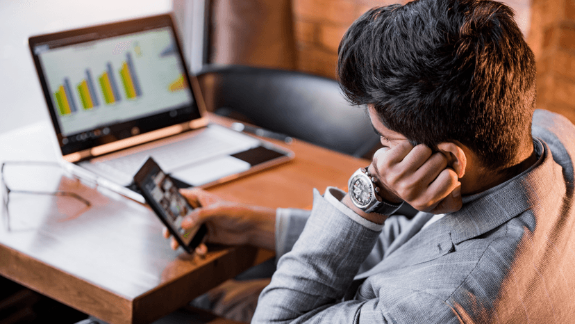frustrated business man looking at cell phone, lap top on the desk in the background