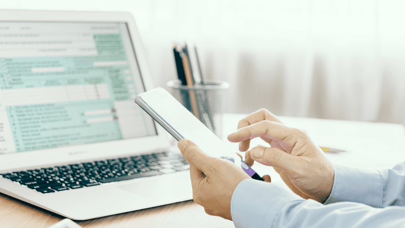 business man looking at mobile device at desk with tax forms pn laptop