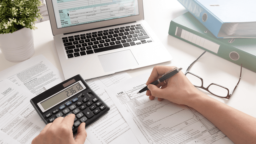 business person looking at mobile device at desk with tax forms on laptop