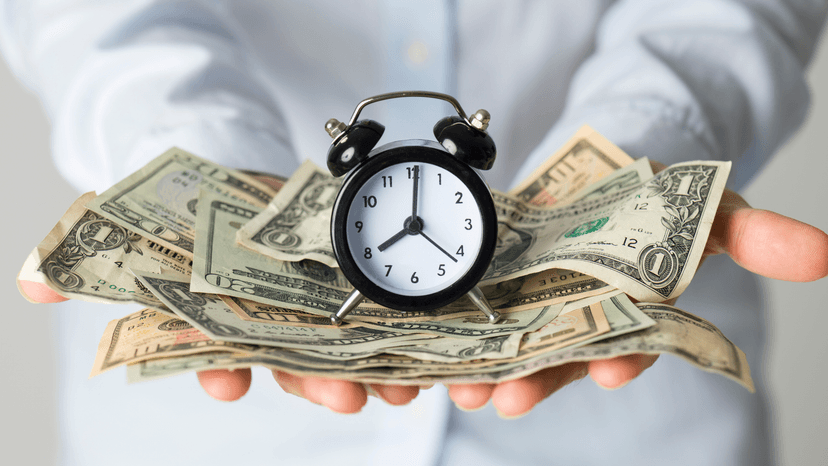 person holding a clock and a pile of cash in various denominations