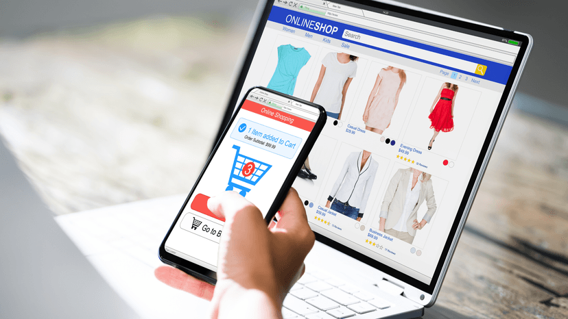 hand holding mobile phone shopping online, in front of laptop also shopping online