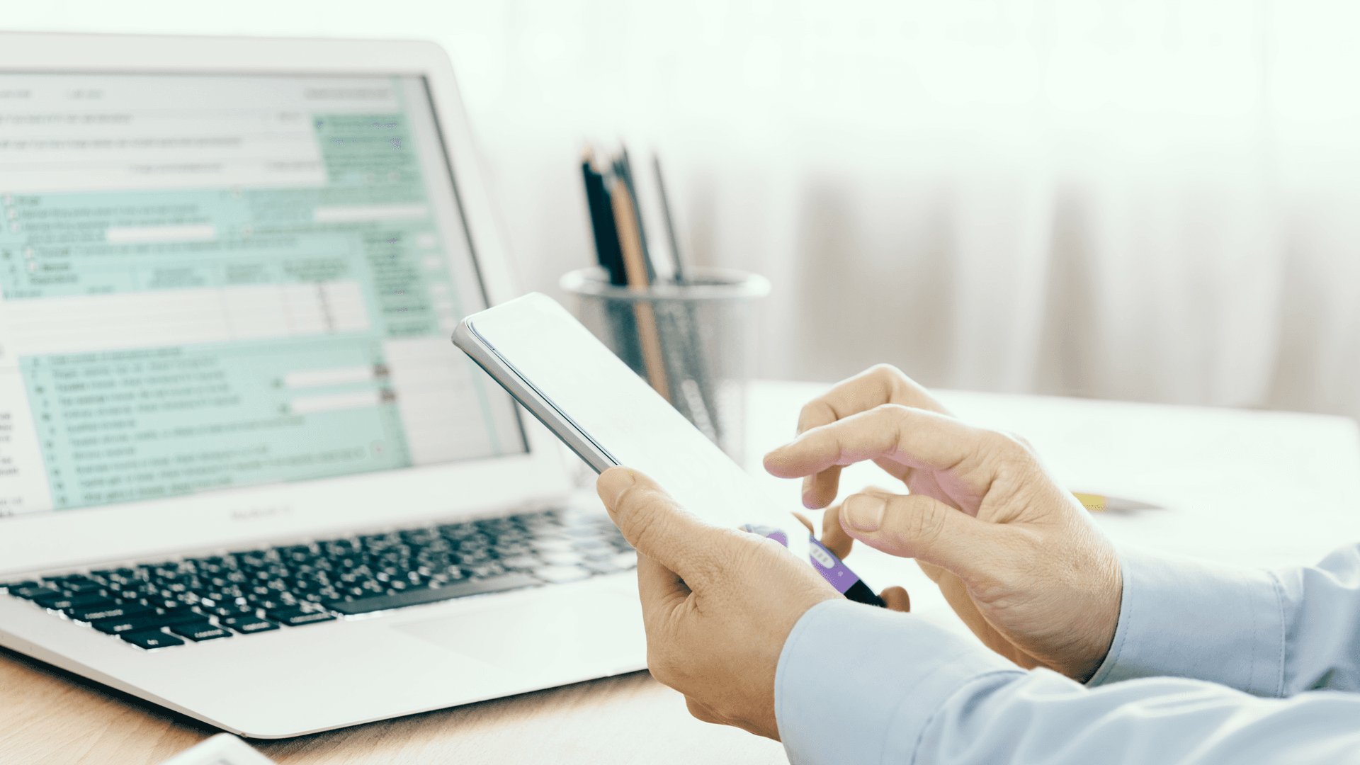 business man looking at mobile device at desk with tax forms pn laptop